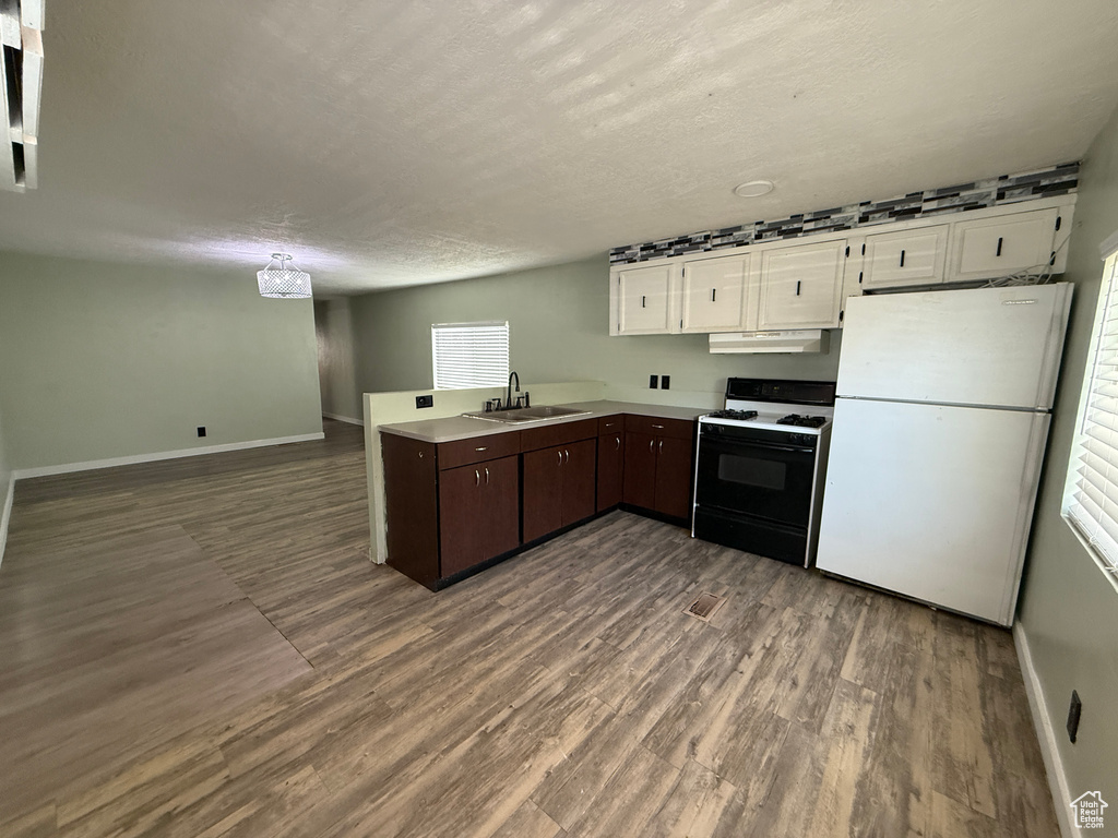 Kitchen with gas range oven, freestanding refrigerator, baseboards, under cabinet range hood, and a textured ceiling