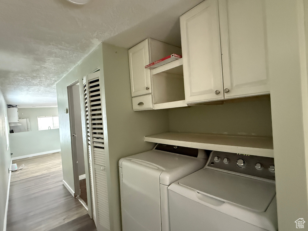 Laundry area featuring cabinet space, washing machine and clothes dryer, wood finished floors, baseboards, and a textured ceiling