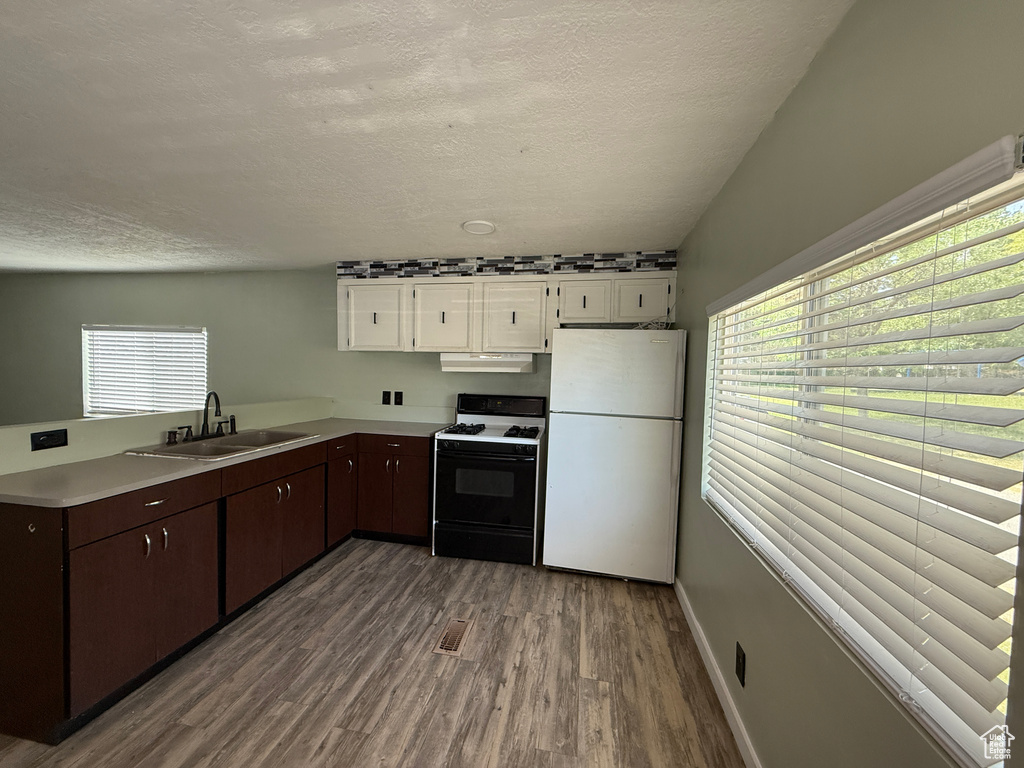 Kitchen with freestanding refrigerator, gas range, a sink, wood finished floors, and white cabinetry