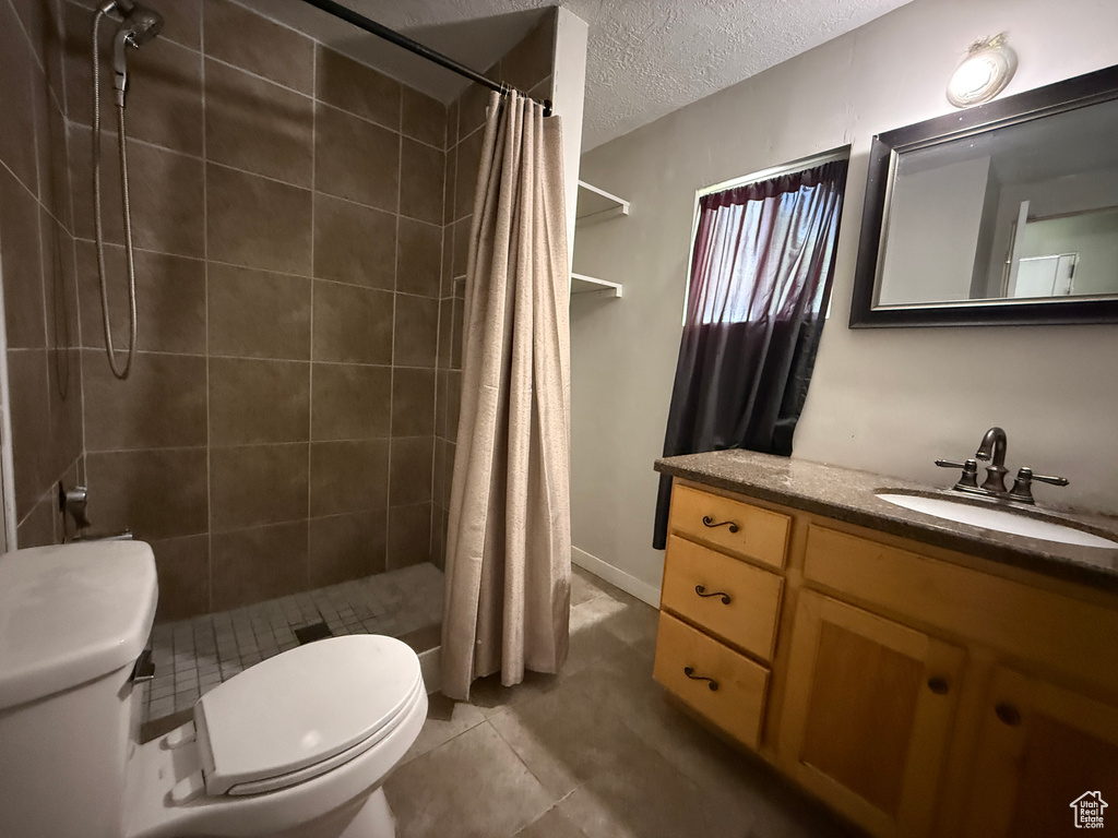 Full bathroom featuring toilet, vanity, tiled shower, a textured ceiling, and tile patterned floors