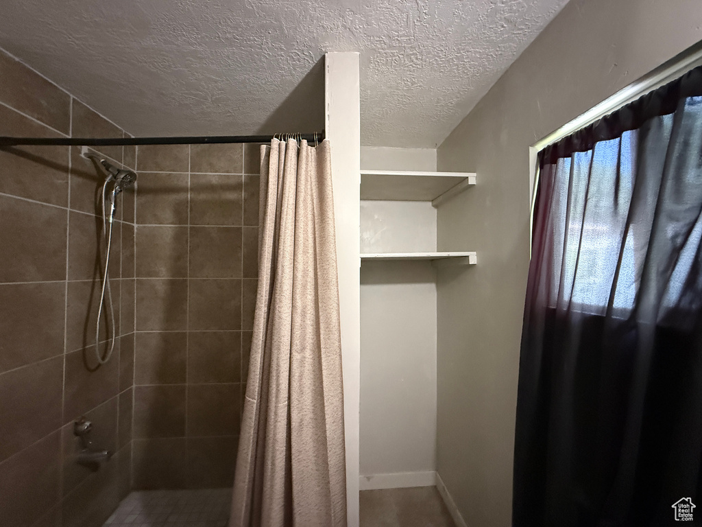 Full bath featuring tiled shower, a textured ceiling, and baseboards