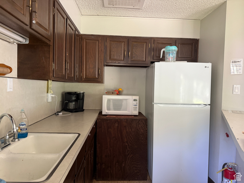 Kitchen featuring white appliances, a sink, dark brown cabinetry, light countertops, and a textured ceiling
