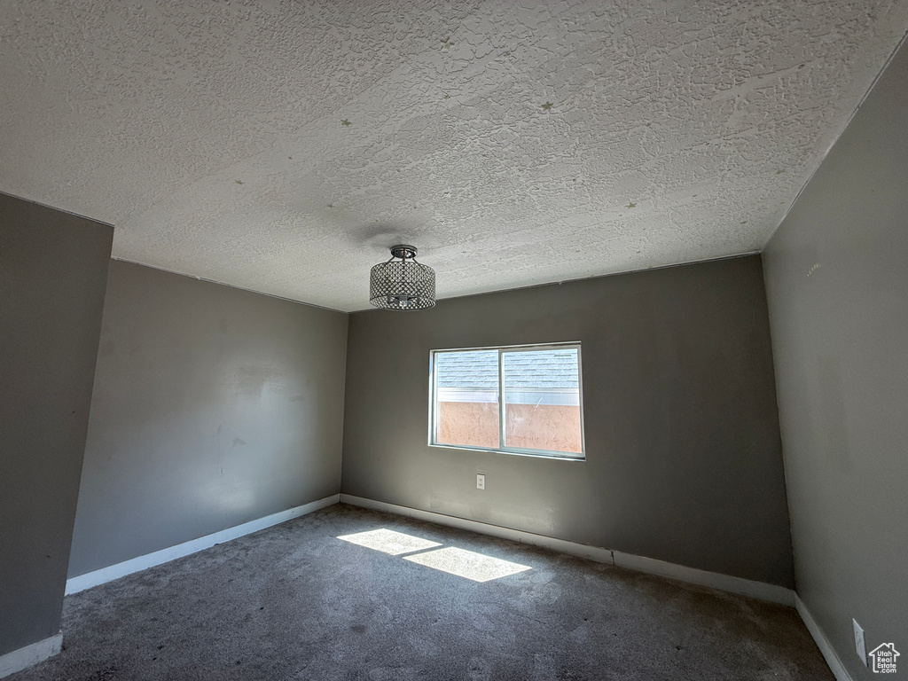 Carpeted empty room featuring a textured ceiling and baseboards