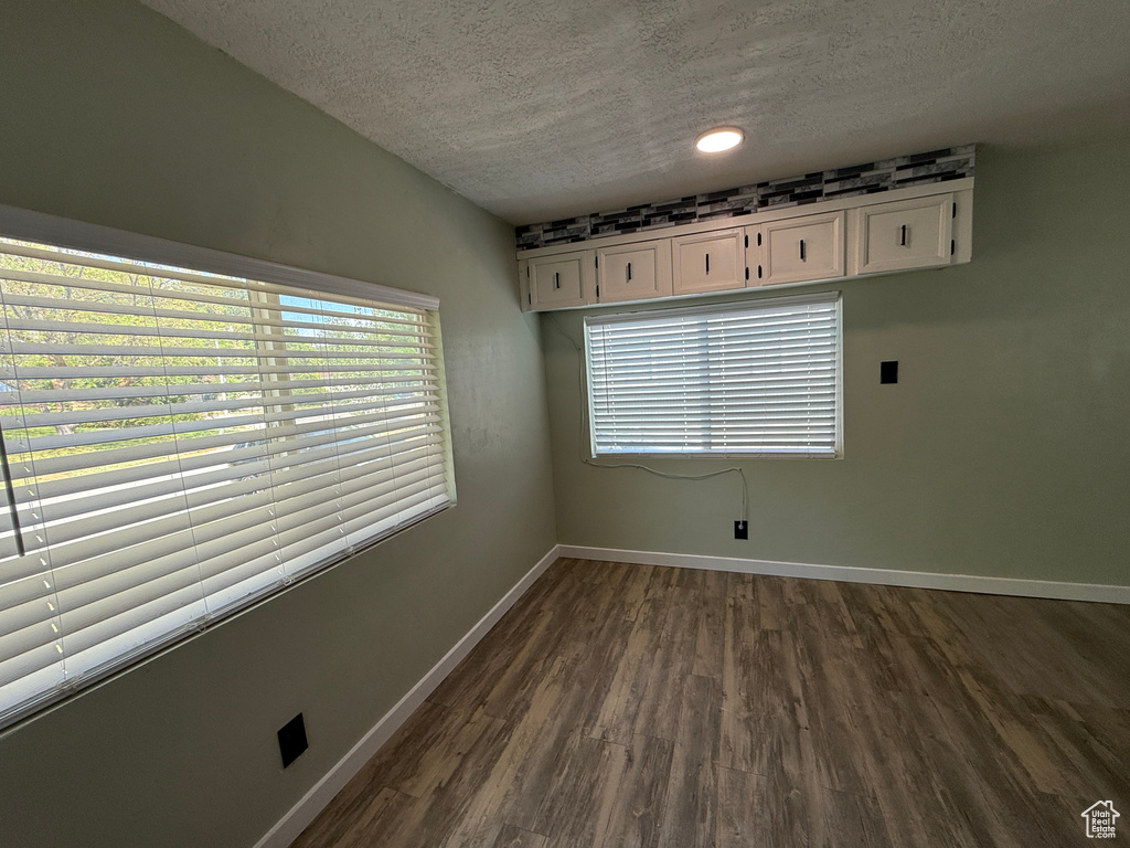 Spare room with a textured ceiling, baseboards, dark wood-style floors, and plenty of natural light
