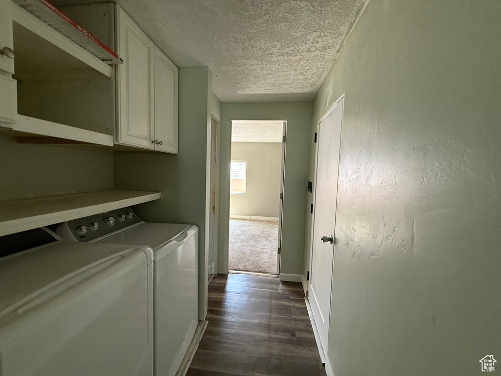 Laundry room featuring washing machine and clothes dryer, cabinet space, dark wood-style floors, a textured ceiling, and baseboards