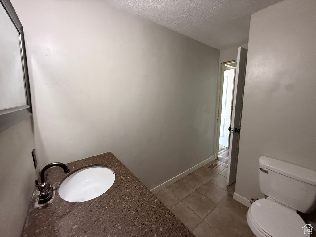 Bathroom featuring toilet, a textured ceiling, tile patterned flooring, baseboards, and vanity