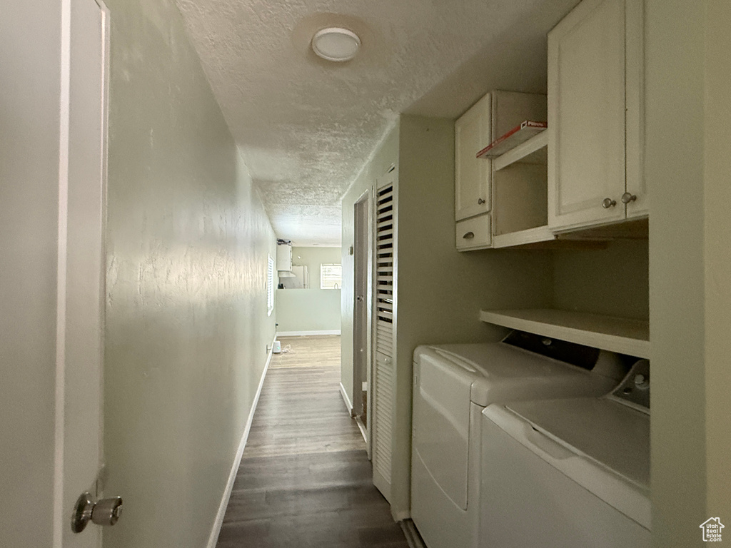 Laundry room with cabinet space, a textured ceiling, washing machine and clothes dryer, wood finished floors, and baseboards