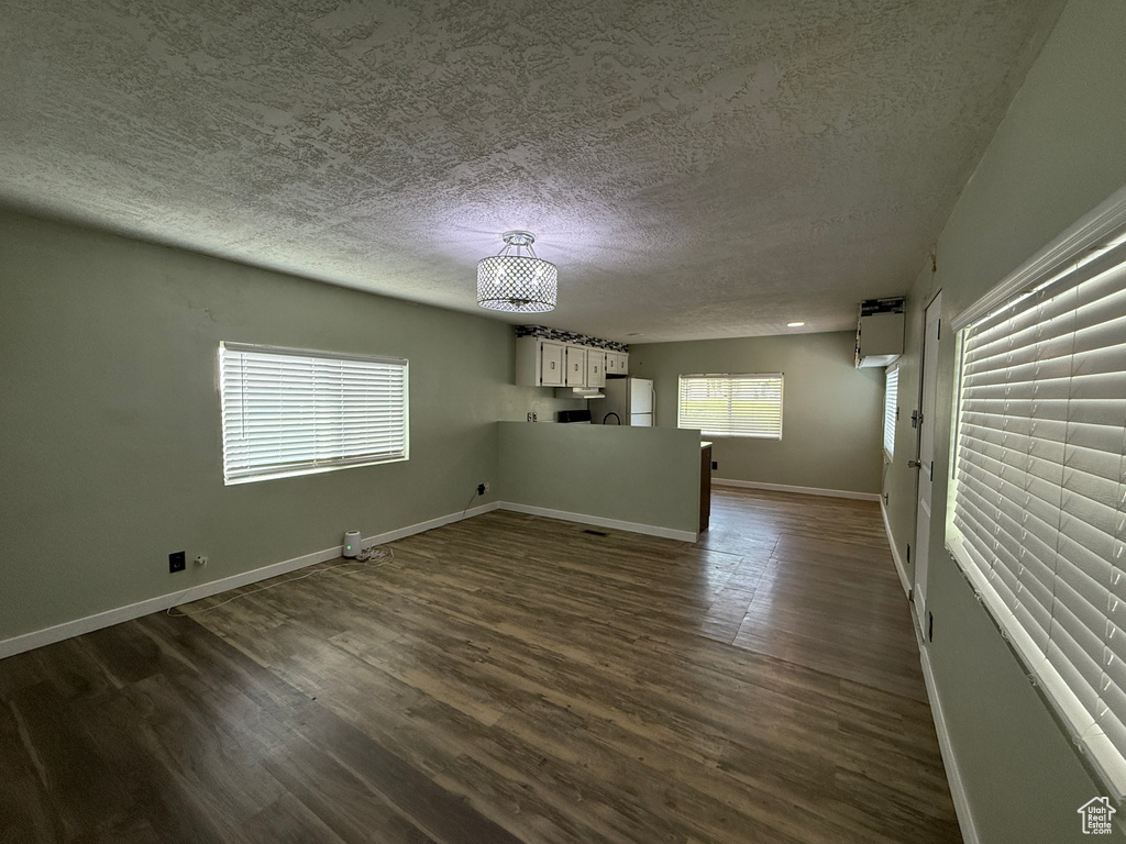 Empty room with a textured ceiling, dark wood-style flooring, and baseboards