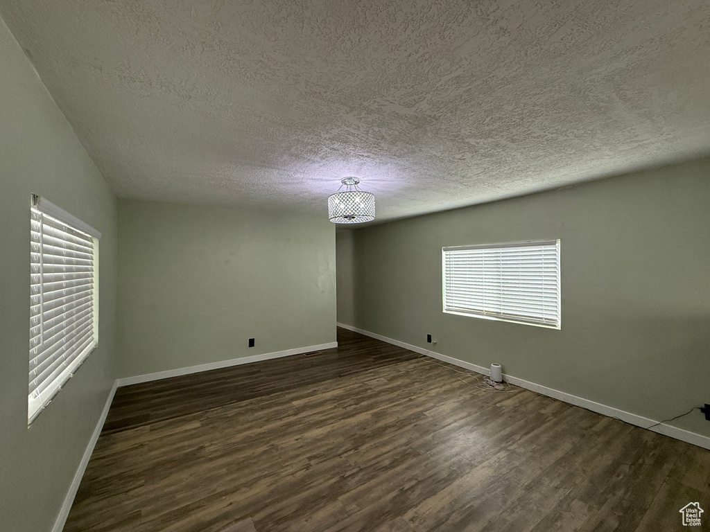 Unfurnished room featuring a textured ceiling, baseboards, and dark wood-style floors