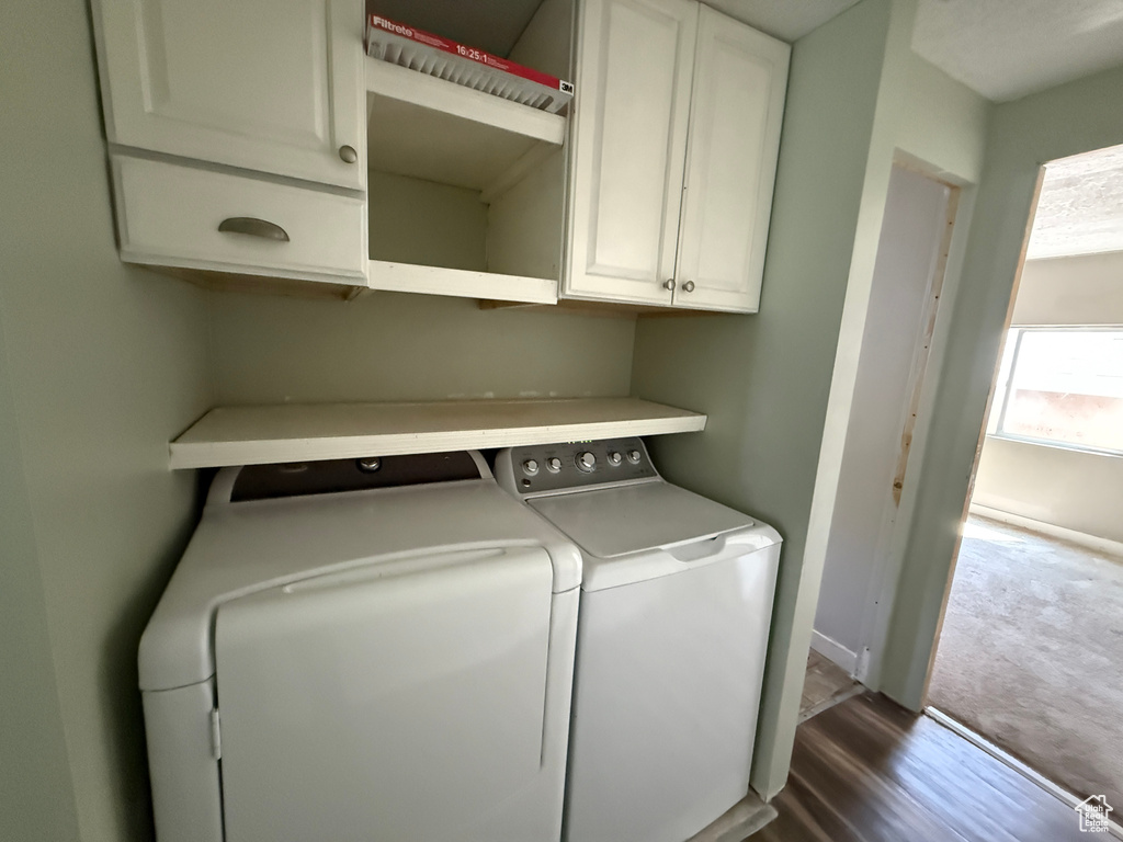 Laundry area featuring washing machine and dryer, cabinet space, and dark wood-style flooring