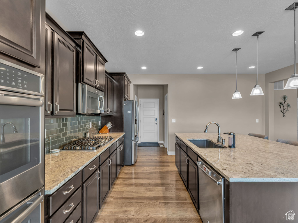 Kitchen featuring a sink, stainless steel appliances, baseboards, a center island with sink, and wood finished floors