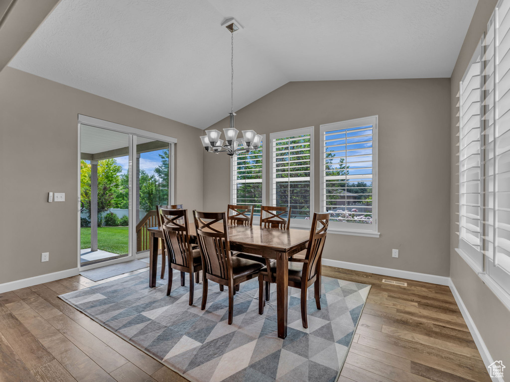 Dining room featuring hardwood / wood-style floors, a chandelier, lofted ceiling, and baseboards