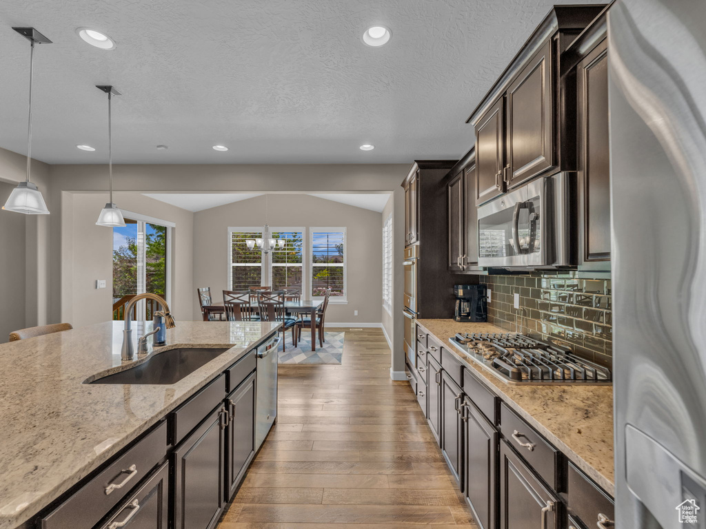 Kitchen with appliances with stainless steel finishes, a sink, baseboards, dark brown cabinetry, and pendant lighting