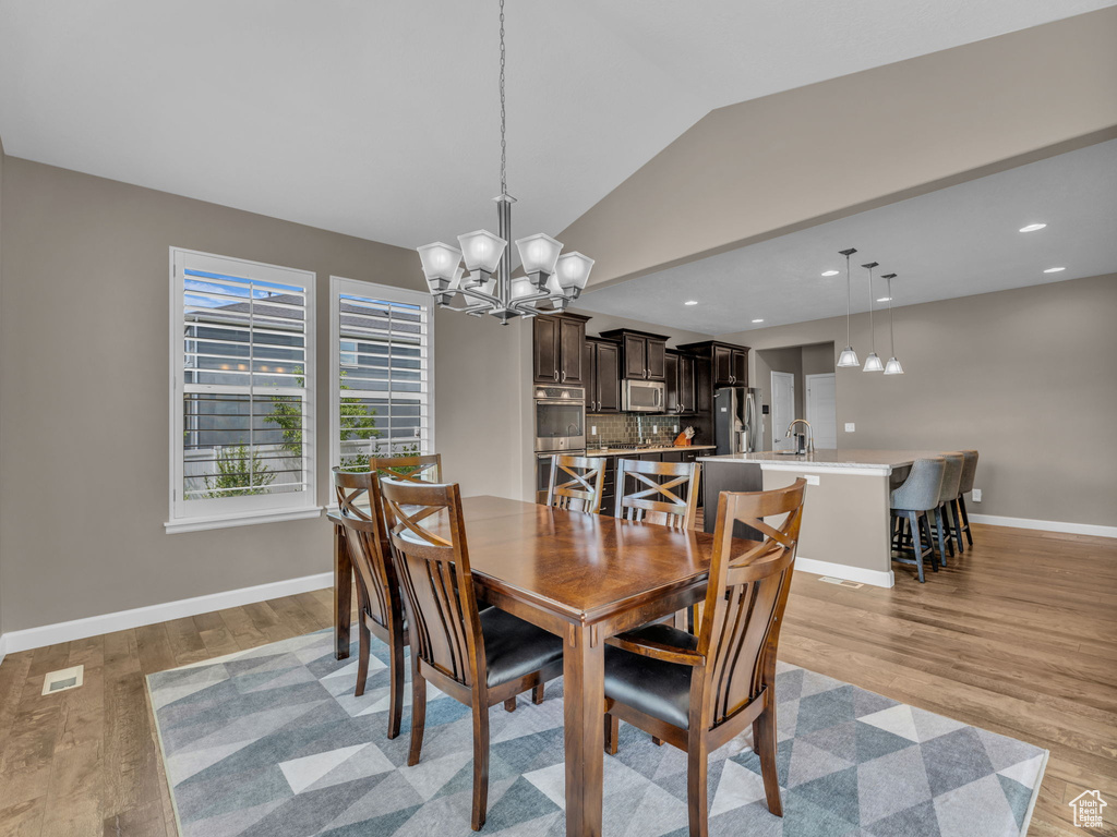 Dining room with a chandelier, lofted ceiling, light wood-type flooring, baseboards, and recessed lighting