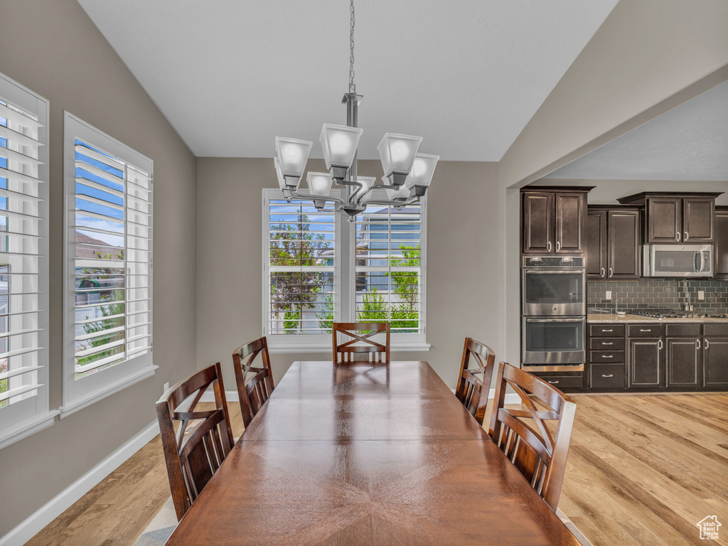 Dining area featuring healthy amount of natural light, light wood finished floors, a chandelier, vaulted ceiling, and baseboards