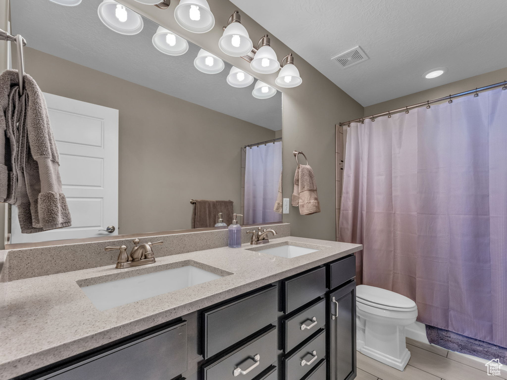 Bathroom with toilet, double vanity, tile patterned floors, and a shower with curtain