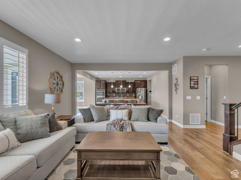 Living area featuring recessed lighting, light wood finished floors, baseboards, and a textured ceiling