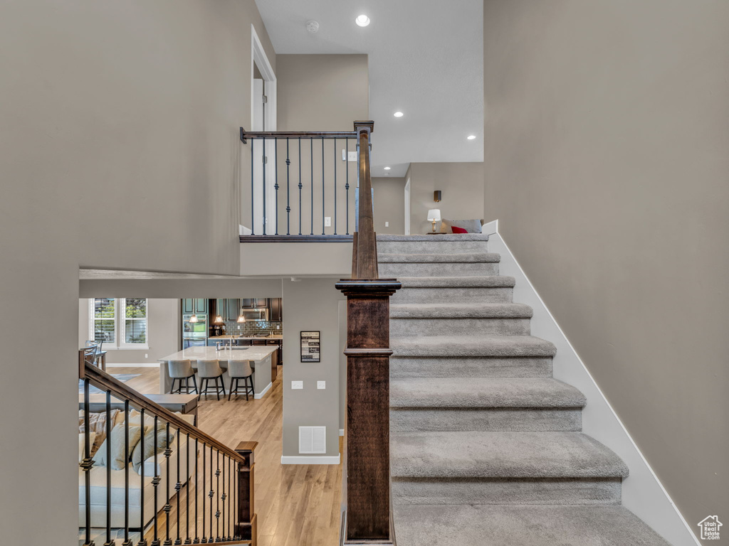 Stairs featuring wood finished floors, a towering ceiling, recessed lighting, and baseboards