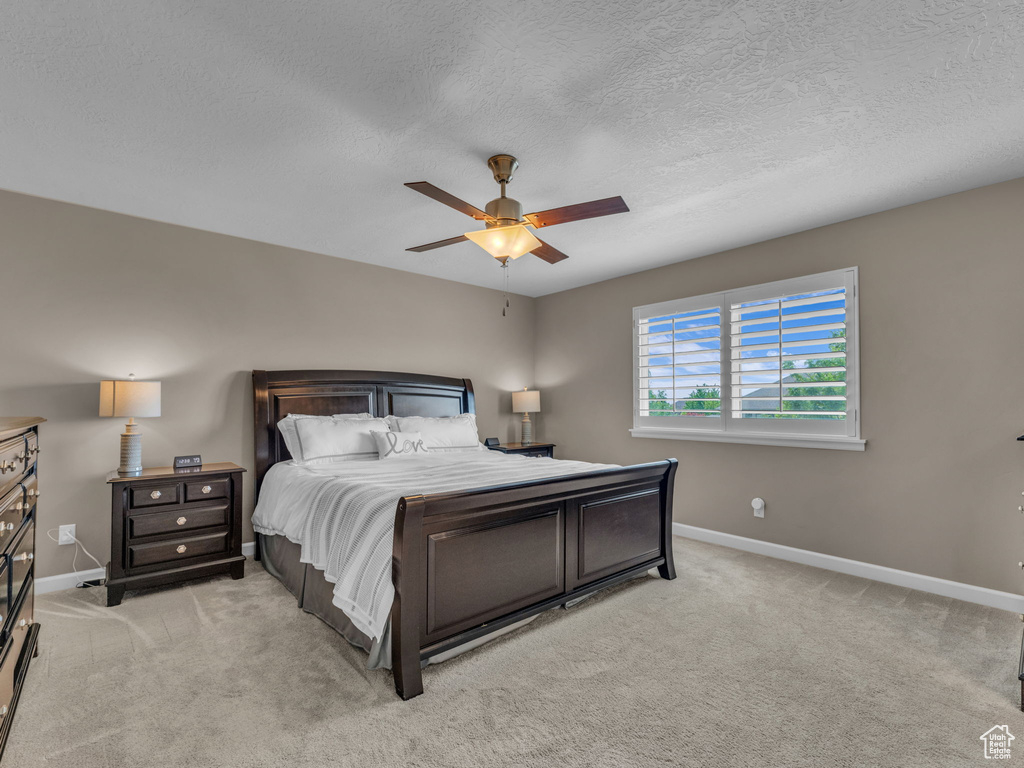 Bedroom with baseboards, light carpet, ceiling fan, and a textured ceiling