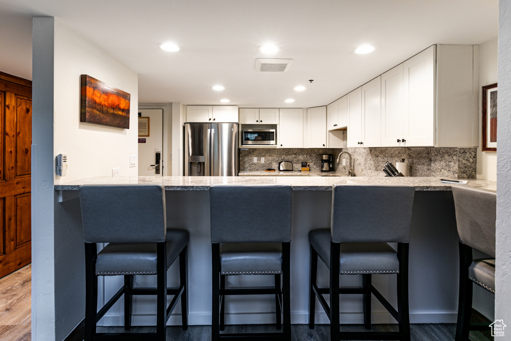 Kitchen featuring stainless steel appliances, a peninsula, white cabinetry, backsplash, and recessed lighting