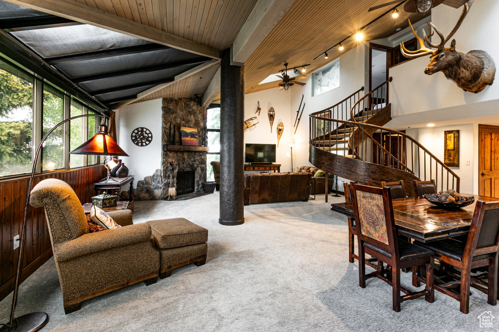 Dining room with a ceiling fan, carpet, stairway, a stone fireplace, and wood ceiling with exposed beams