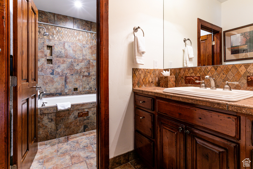 Bathroom featuring vanity, stone tile flooring, tasteful backsplash, and tiled shower / bath