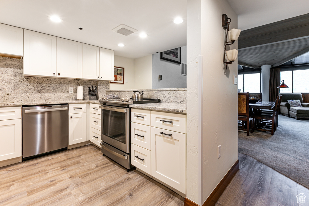 Kitchen featuring stainless steel appliances, light wood finished floors, white cabinetry, backsplash, and light stone countertops