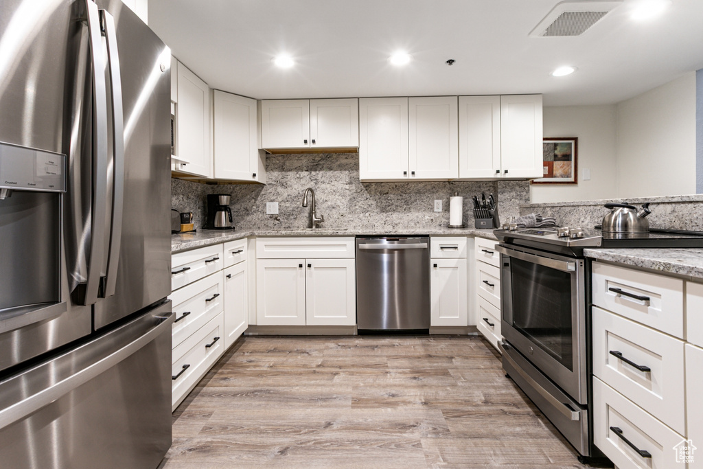 Kitchen featuring stainless steel appliances, a sink, white cabinets, light stone countertops, and light wood finished floors