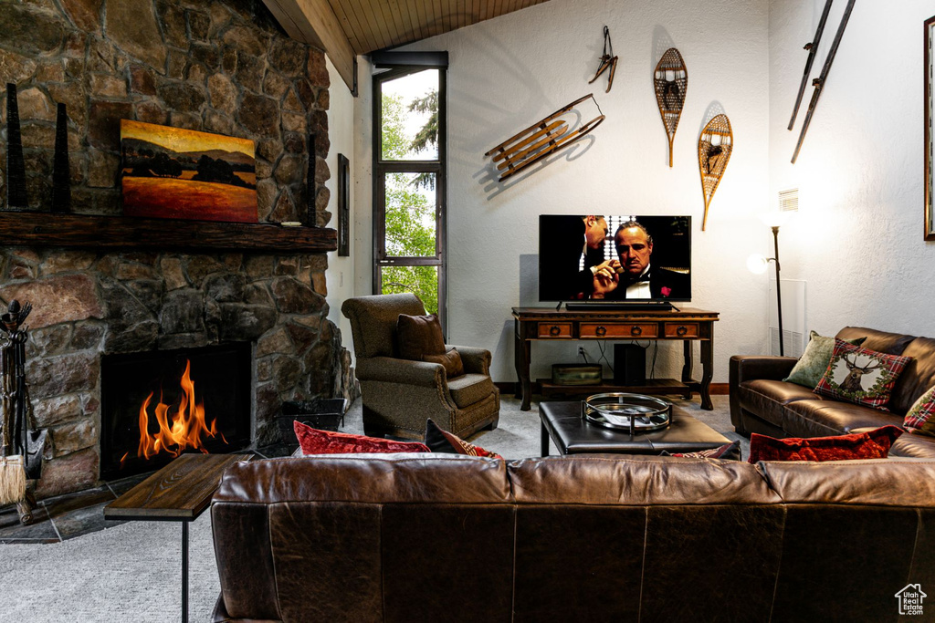 Carpeted living area featuring vaulted ceiling, a stone fireplace, wooden ceiling, and baseboards