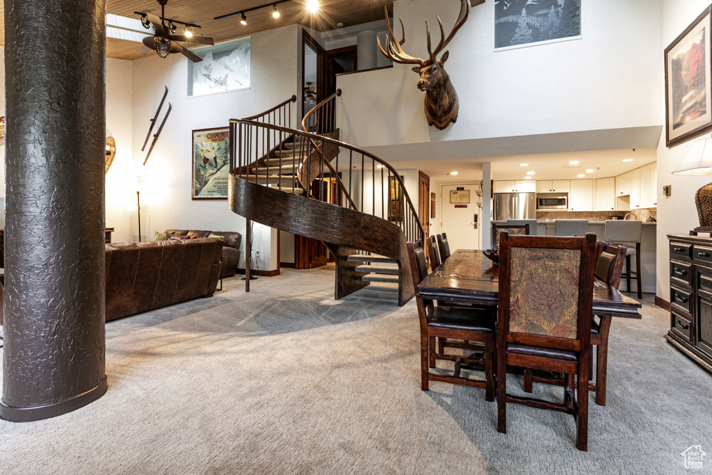 Dining area with light colored carpet, stairway, a high ceiling, and track lighting