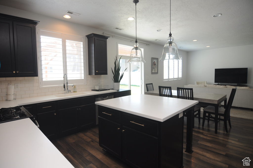 Kitchen with a sink, dark cabinets, dark wood-style floors, tasteful backsplash, and light countertops