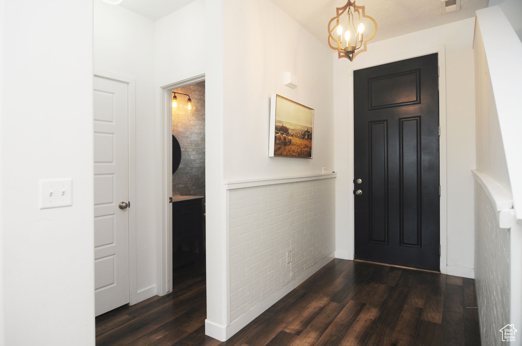 Foyer featuring dark wood-type flooring, a chandelier, and wainscoting