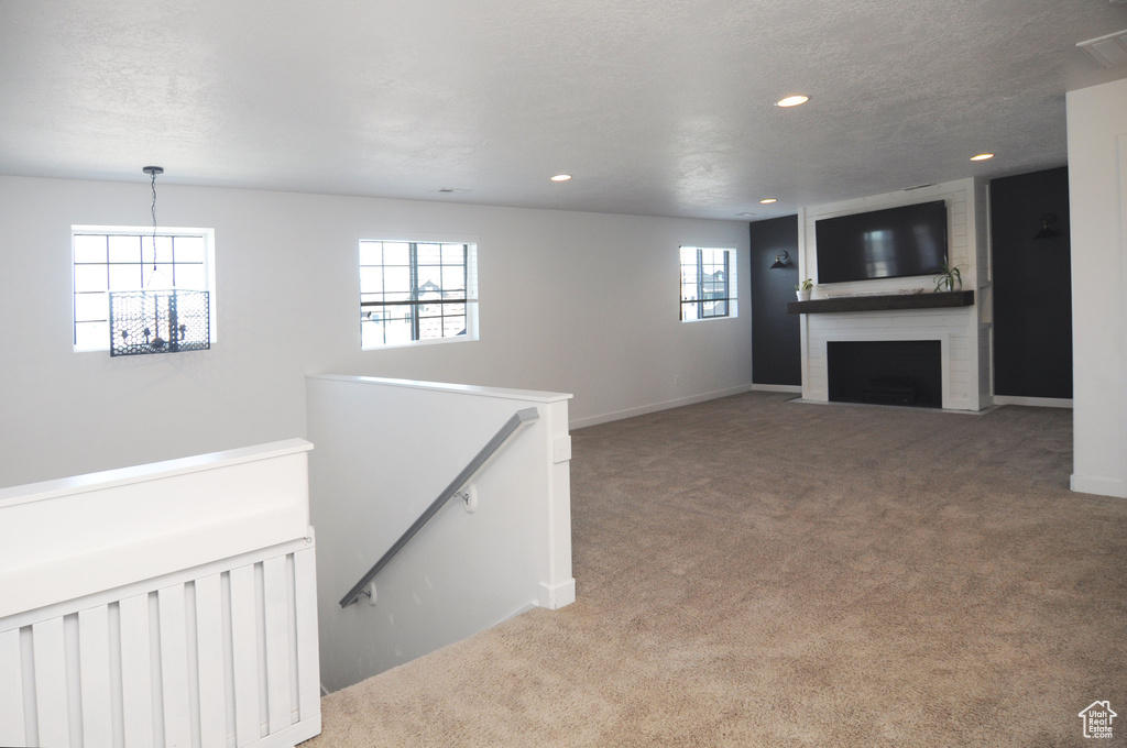 Unfurnished living room featuring carpet floors, recessed lighting, a large fireplace, baseboards, and a chandelier
