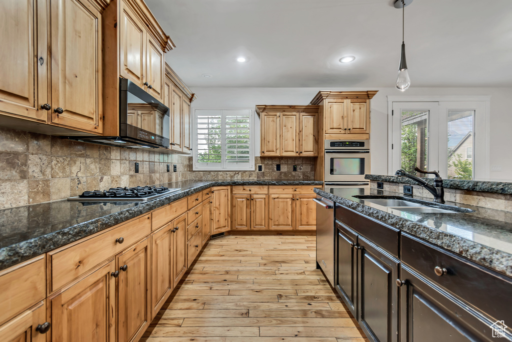 Kitchen with a sink, appliances with stainless steel finishes, light wood-type flooring, dark stone counters, and recessed lighting