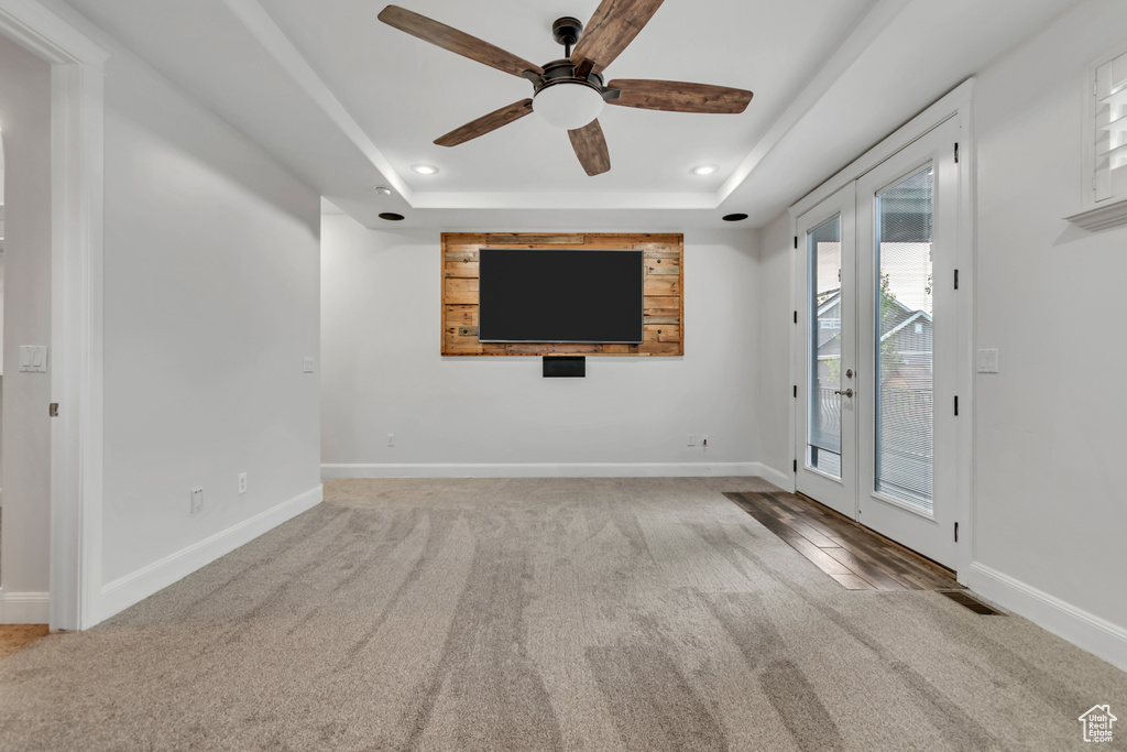 Unfurnished living room featuring carpet floors, a tray ceiling, recessed lighting, ceiling fan, and baseboards