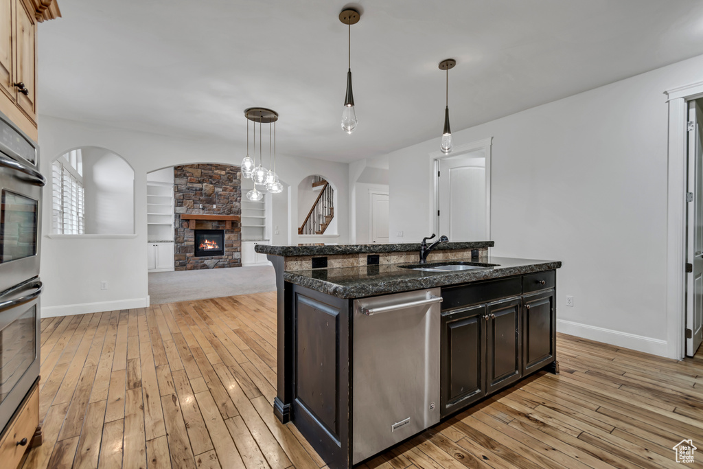 Kitchen featuring stainless steel appliances, a sink, a stone fireplace, light wood-style flooring, and baseboards