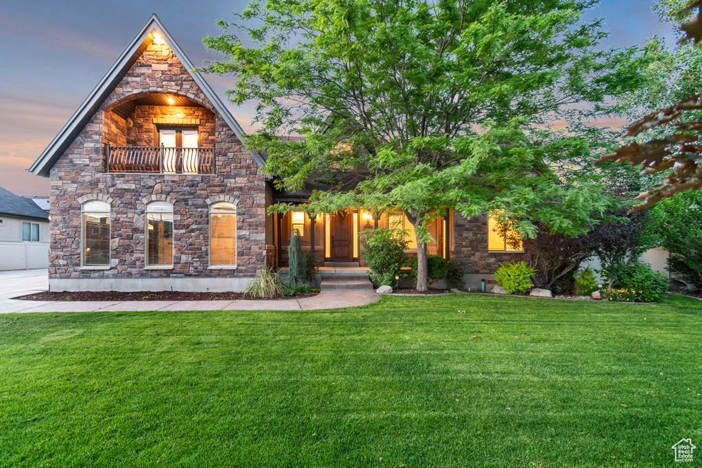View of front of property with stone siding, a front lawn, and a balcony