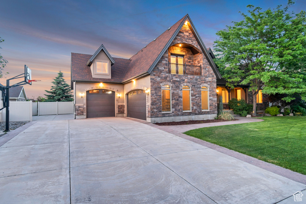 View of front of house featuring stone siding, a balcony, concrete driveway, and a garage