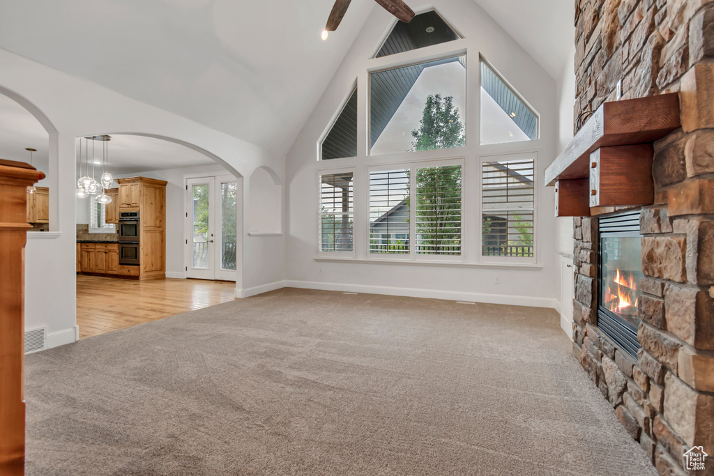 Unfurnished living room featuring a stone fireplace, high vaulted ceiling, light carpet, arched walkways, and baseboards