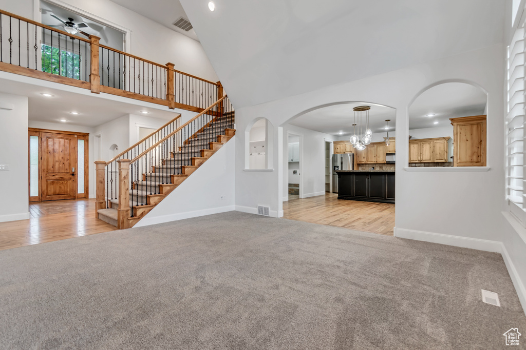 Unfurnished living room with light colored carpet, a towering ceiling, stairway, baseboards, and recessed lighting