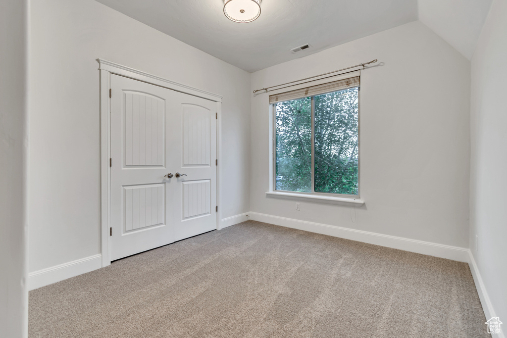 Unfurnished bedroom with light carpet, baseboards, a closet, and lofted ceiling