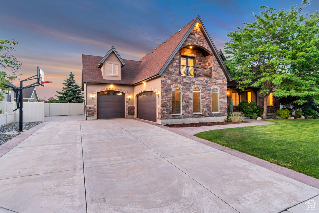 View of front facade with stone siding, concrete driveway, a balcony, a garage, and stucco siding