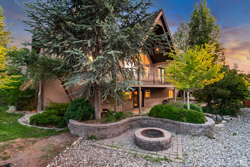 Back of property at dusk with a patio, an outdoor fire pit, stucco siding, and a balcony