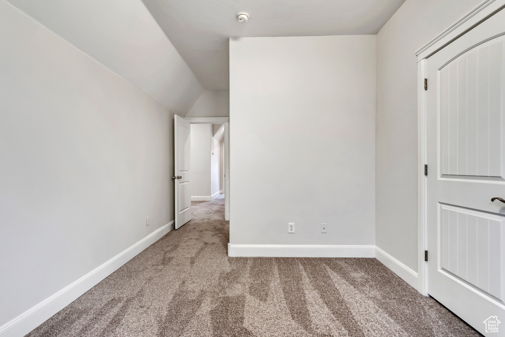 Unfurnished bedroom featuring carpet, baseboards, and vaulted ceiling
