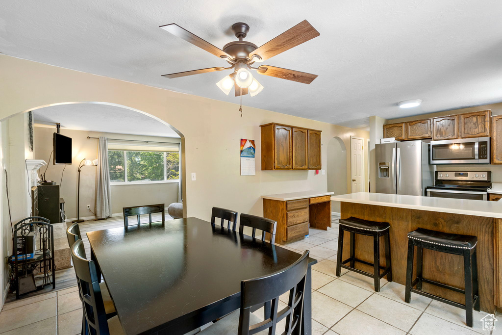 Dining space with arched walkways, light tile patterned flooring, and a ceiling fan