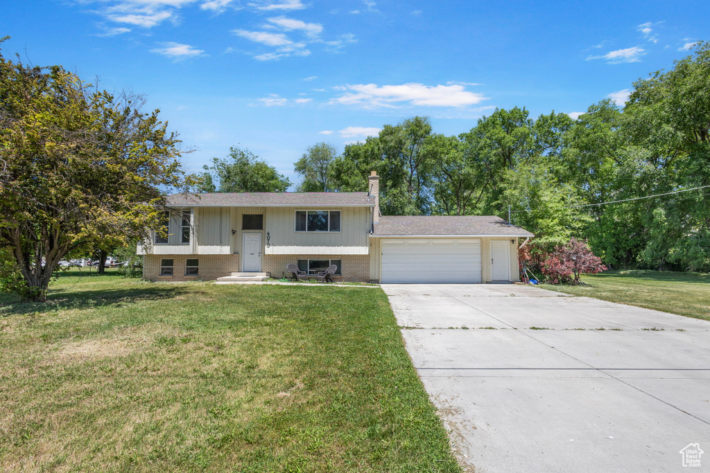 Bi-level home featuring a garage, a front lawn, driveway, and brick siding