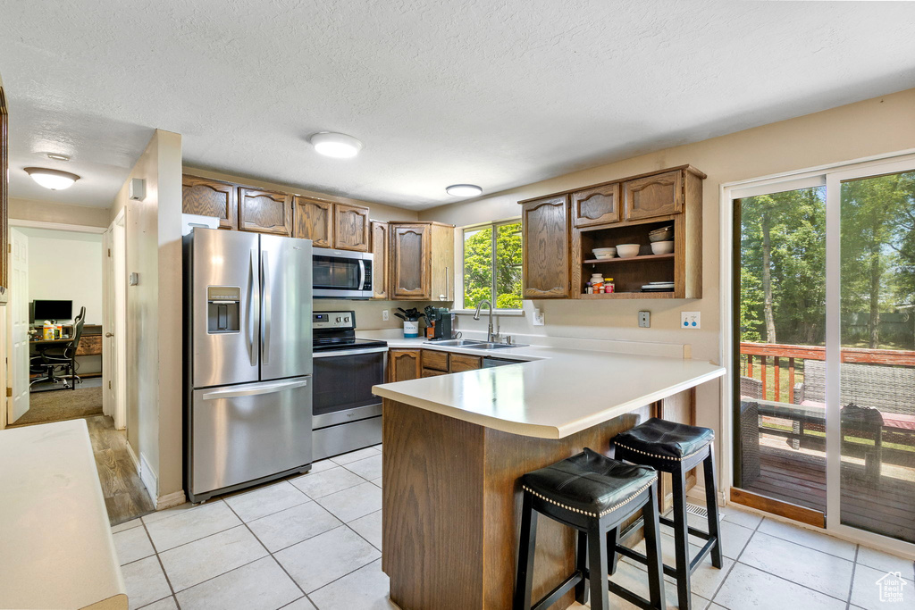 Kitchen with stainless steel appliances, a peninsula, a sink, a breakfast bar, and light tile patterned floors