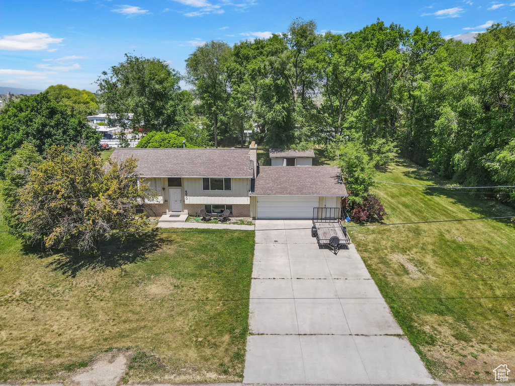 Raised ranch featuring concrete driveway, roof with shingles, a front lawn, and an attached garage