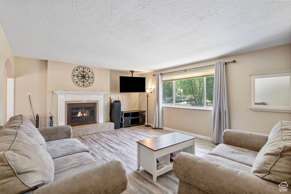 Living area featuring a textured ceiling, light wood finished floors, a premium fireplace, arched walkways, and baseboards