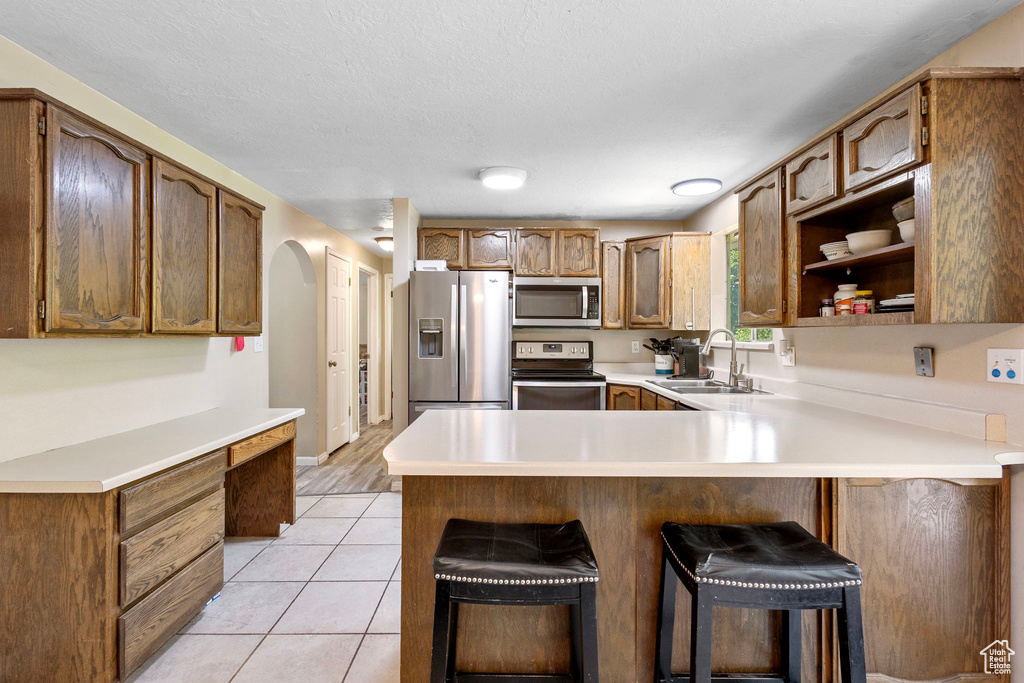 Kitchen featuring stainless steel appliances, a sink, a peninsula, arched walkways, and light countertops